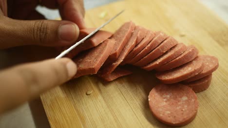 close up of someone slicing red salami with a knife