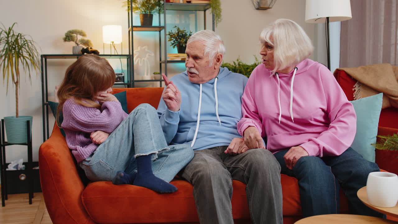 Irritated grandfather and grandmother scolding granddaughter child kid for bad behavior on home sofa