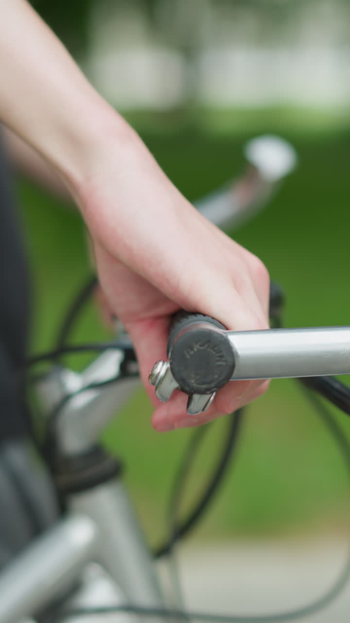 vista parcial de una persona con camiseta negra caminando a lo largo de su bicicleta bicicleta en un camino pacífico, centrándose en la mano agarrando el manillar de la bicicleta, la escena está rodeada de vegetación