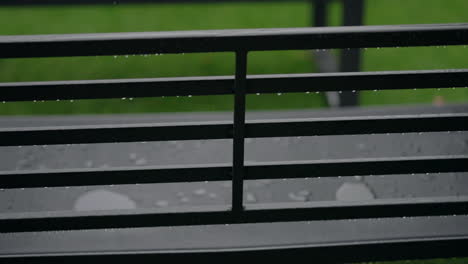 Raindrops-on-a-metal-railing,-with-a-blurred-green-background,-capturing-the-essence-of-a-rainy-day