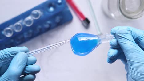 scientist handling a blue liquid in a flask with pipette in a lab