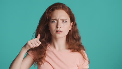 Redheaded-concerned-girl-in-front-of-camera-on-turquoise-background.