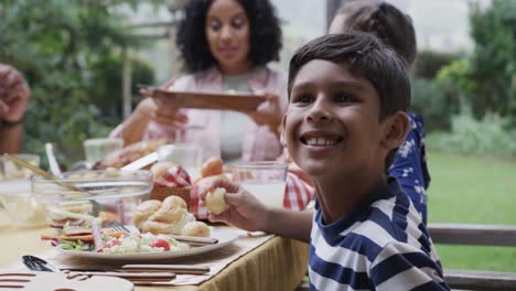 Happy-biracial-parents,-son-and-daughter-eating-meal-at-dinner-table-in-garden,-slow-motion