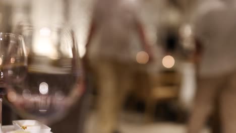 escena borrosa del restaurante con copas de vino y camareros, capturando una cálida y acogedora atmósfera nocturna
