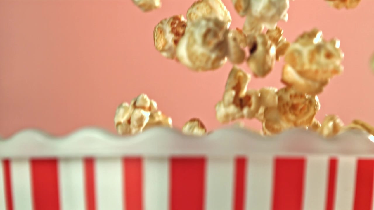 Popcorn al caramello che cadono in una scatola di popcorn a strisce al rallentatore