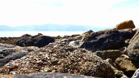 Colourful-variety-of-stone-boulders-beach-landscape-under-North-Wales-mountain-range-lowering-jib-shot