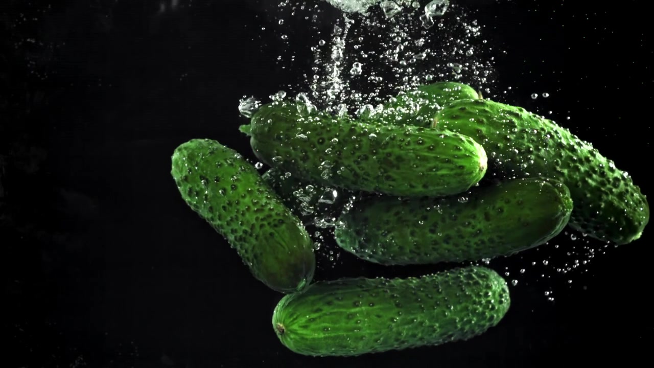 Fresh Green Cucumbers Splashing into Water in Slow Motion