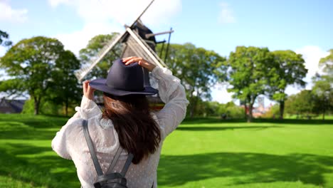 rear view of woman looking at windmill on a windy day in denmark, puts on hat