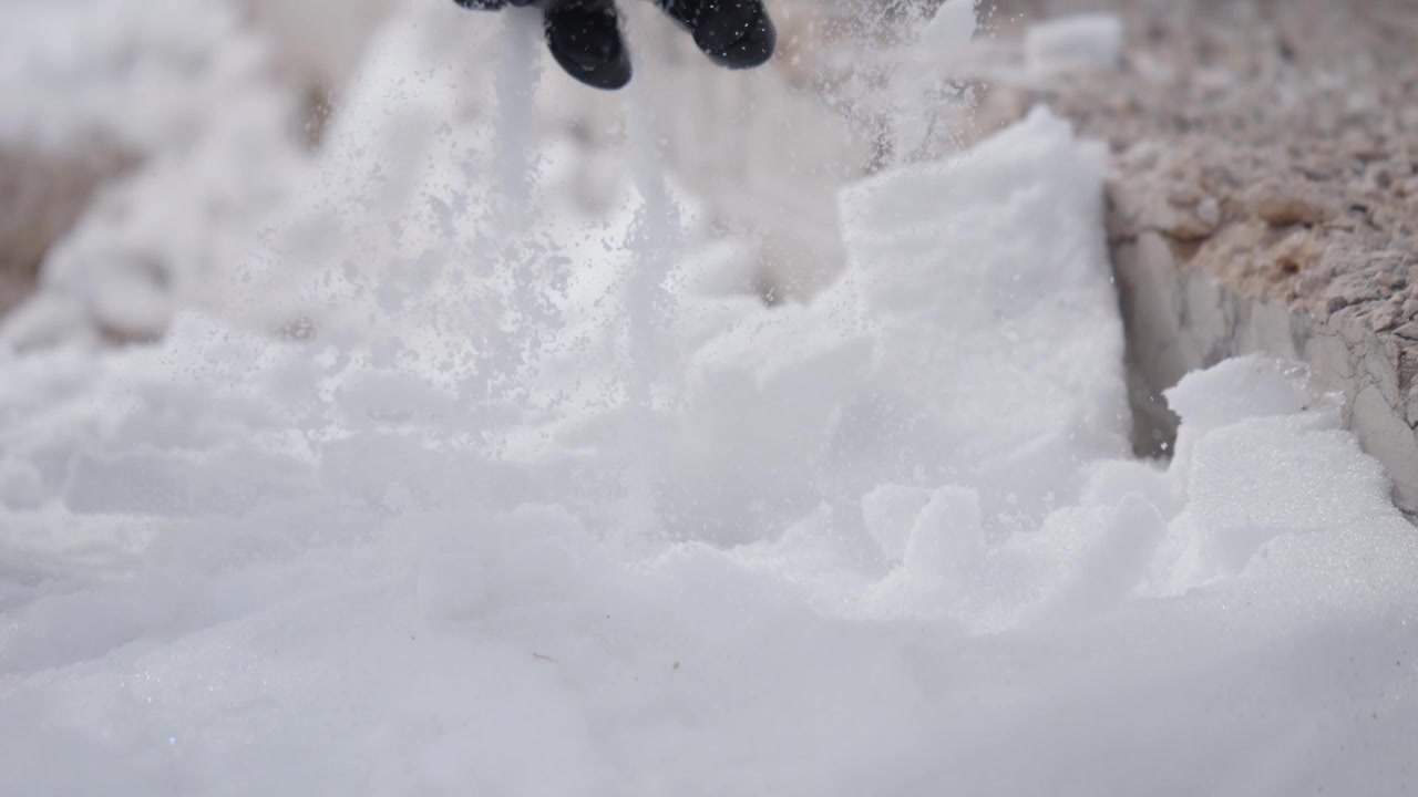 Frischer Schnee schießt in Zeitlupe in die Luft und verstreut eisige Partikel und Pulver über eine helle Winterlandschaft in einer dynamischen Nahaufnahme.