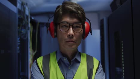 portrait of asian male it technician wearing headphones by computer server