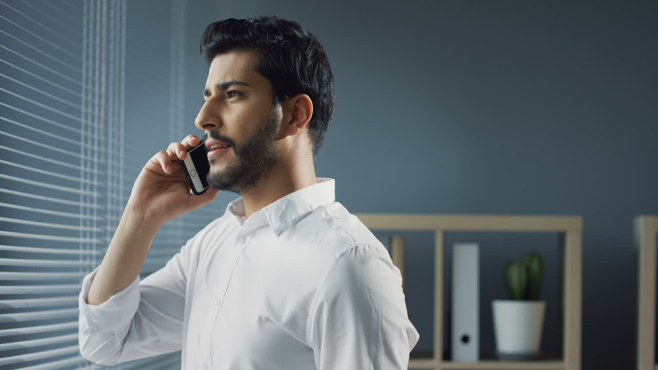 멋진 사무실에 서서 전화를 받고 창밖을 내다보는 아라비아 사업가의 시야를 닫습니다