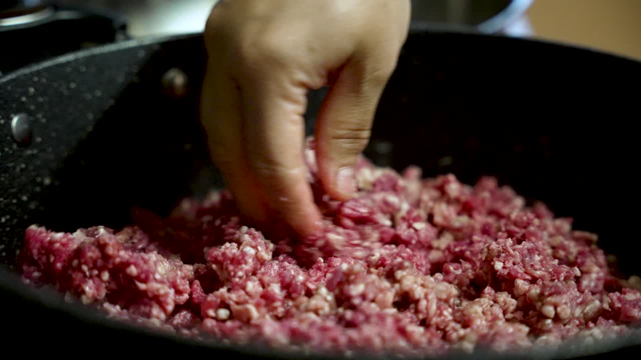 Koki mencampur daging sapi cincang mentah dengan tangan kosong di dapur profesional, menonjolkan seni persiapan makanan dan keterampilan kuliner
