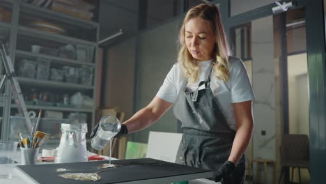 woman pouring resin on canvas in art studio