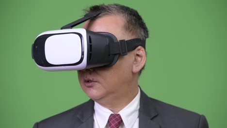 mature japanese businessman using virtual reality headset against green background