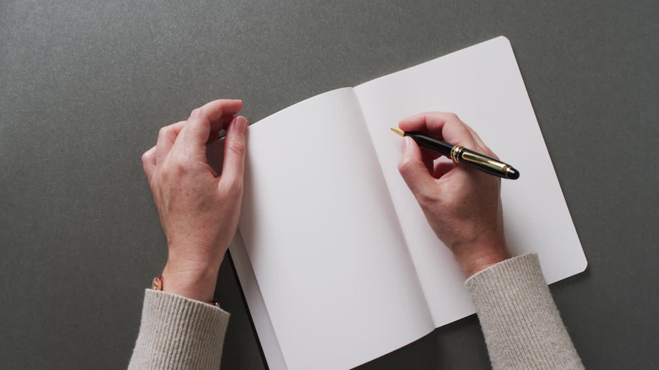 Close up of hands writing with pen on book with copy space on gray background in slow motion