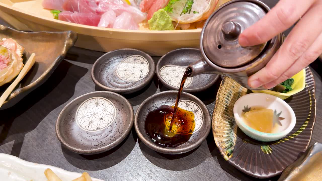 新鮮な刺身の横にある小皿に、陶器の器から醤油を注ぐ手。
