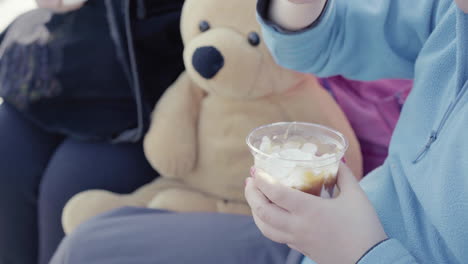 Nahaufnahme-Eines-Kleinen-Mädchens-Mit-Blauem-Pullover,-Nagellack-Und-Teddybär-Neben-Ihr-Mit-Einem-Eisbecher-Im-Freien-4k