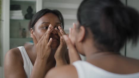 Young-African-American--woman-applying-face-cream-in-the-mirror-reflection.