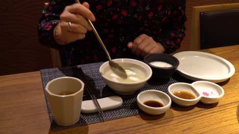 woman eating dongchimi korean radish water kimchi, showing on spoon close-up in restaurant