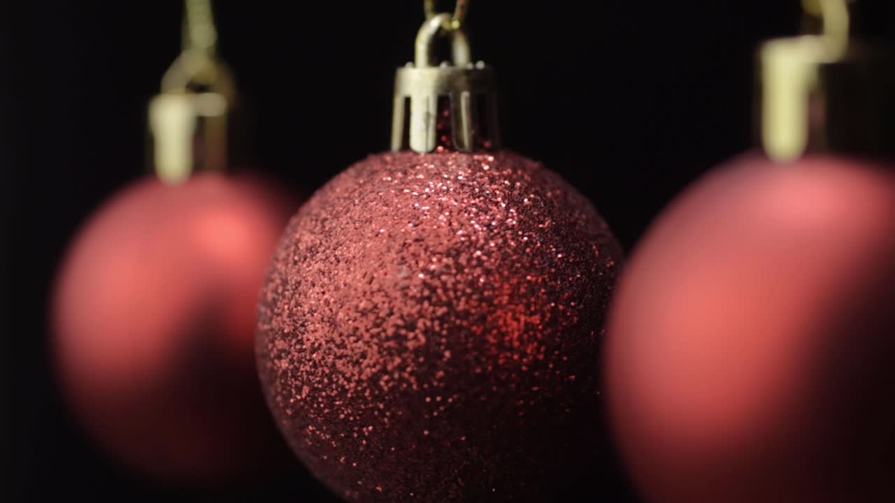 Macro de três enfeites de Natal vermelhos pendurados em um fundo preto