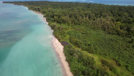 Flight-over-a-paradisiacal-beach-with-turquoise-water-bordered-by-a-jungle