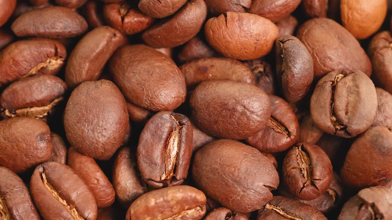 Video ravvicinato di chicchi di caffè che ruotano, evidenziando la texture e il colore sotto un'illuminazione calda.