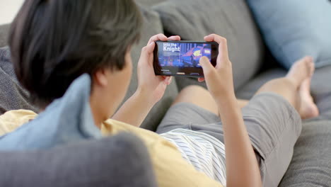 un adolescente asiático juega un juego en su teléfono inteligente en casa