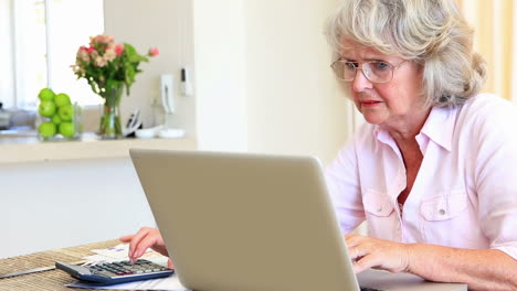 senior woman sitting at table paying her bills with laptop