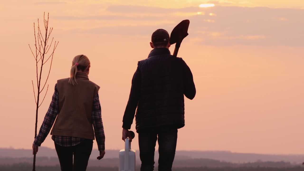 한 쌍의 농부가 묘목과 삽을 들고 나무를 심으러 간다