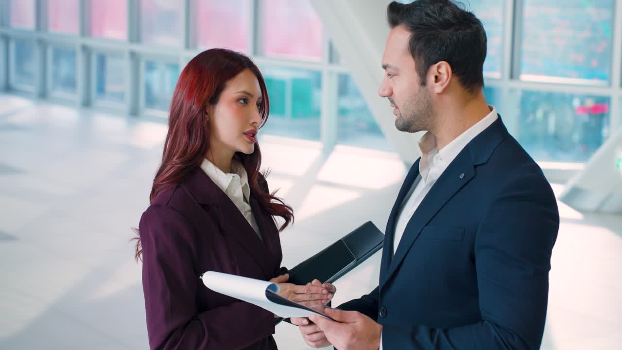 Toma cinematográfica en primer plano medio con efecto paralaje y cámara lenta, orbitando a dos colegas de negocios revisando e intercambiando documentos en un vibrante y moderno vestíbulo corporativo.