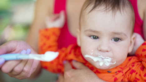 adorable caucasian child being given dairy food from spoon. kid is full and pushes mom's hand away and stretches arms.