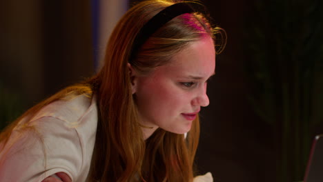 a young woman with blonde hair and a headband smiles while looking at her laptop screen.