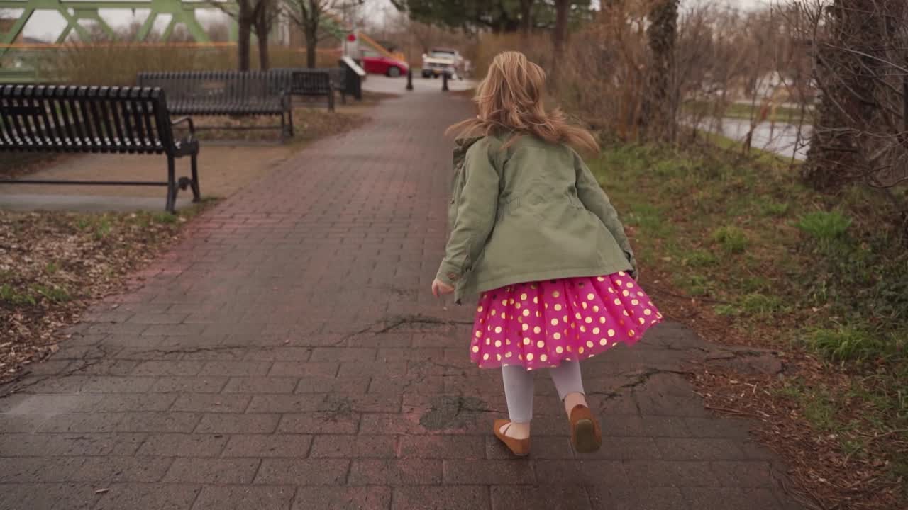 una niña adorable con un vestido rosa corriendo afuera después de una lluvia de primavera - cámara lenta