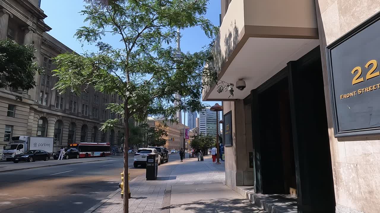 First-person walk Vibrant city scene on Front Street, Toronto, featuring pedestrians, cars, and iconic CN Tower on bright day. Urban architecture and greenery add to lively street ambiance, Canada