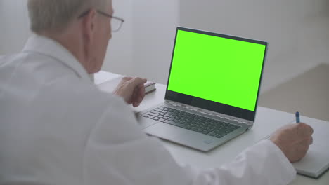 portátil con pantalla verde en la mesa del médico de trabajo el hombre está mirando la pantalla y escribiendo notas concepto de aprendizaje electrónico