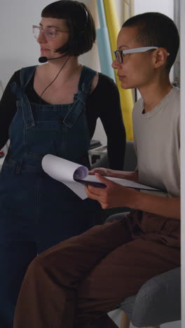 Vertical-Video-Of-Female-Film-Director-And-Assistant-Watching-Actors-And-Checking-Script-Shooting-Movie-Or-Video-Scene-In-Studio