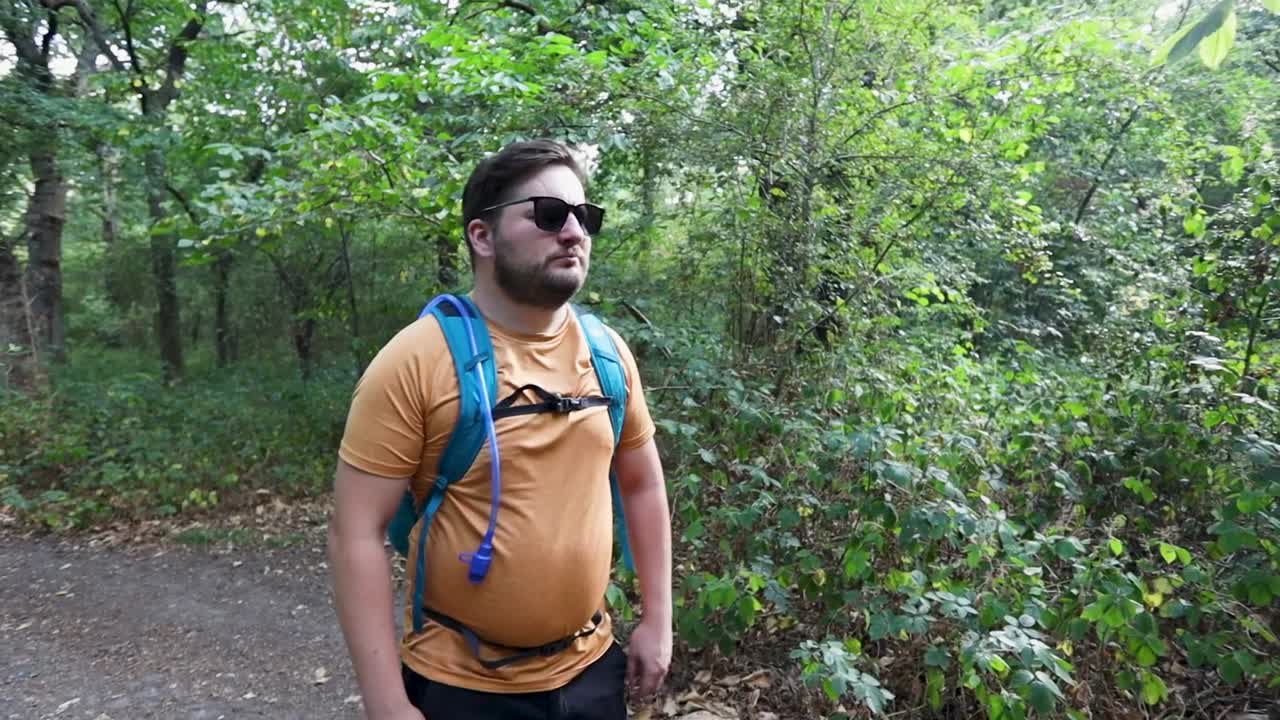 un joven con una mochila y gafas de sol sale del bosque y se da cuenta de que está perdido y luego se aleja