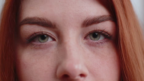 close-up macro portrait of young woman face smiling, redhead girl eyes looking at camera blink wink