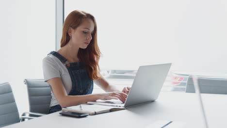 joven mujer de negocios vestida casualmente trabajando en una computadora portátil en una oficina moderna tomando llamadas por teléfono móvil