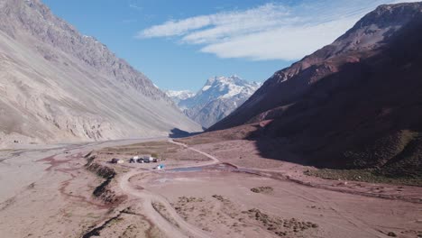 Vista-Aérea-De-La-Carretera-Sin-Pavimentar-Y-El-Río-Volcán-En-La-Cordillera-De-Los-Andes-En-San-Jose-De-Maipo,-Chile