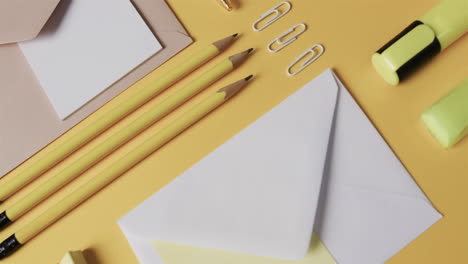 pencils, paper clips, and envelopes are neatly arranged on a pastel yellow surface