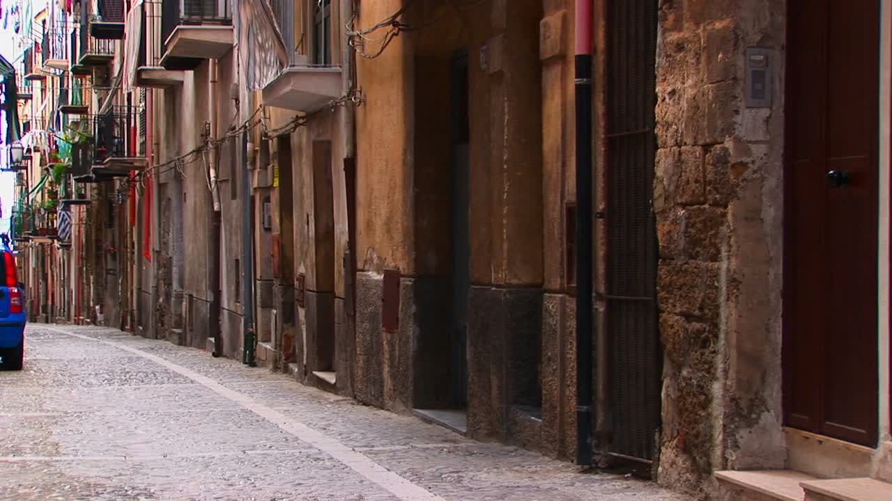 Una calle empedrada cerca de casas y balcones muy juntos en Cefalú, Italia