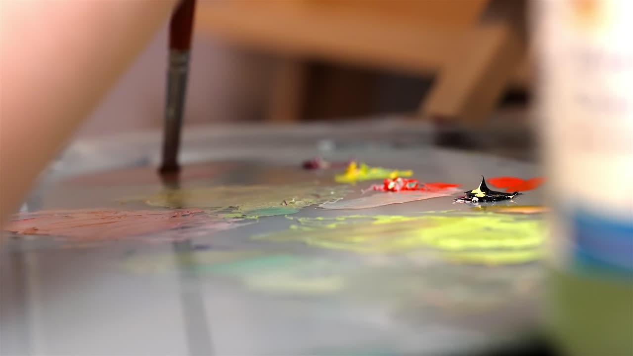 Braccio in primo piano, fuori fuoco, che dipinge prendendo il colore da mucchietti per miscelarlo.