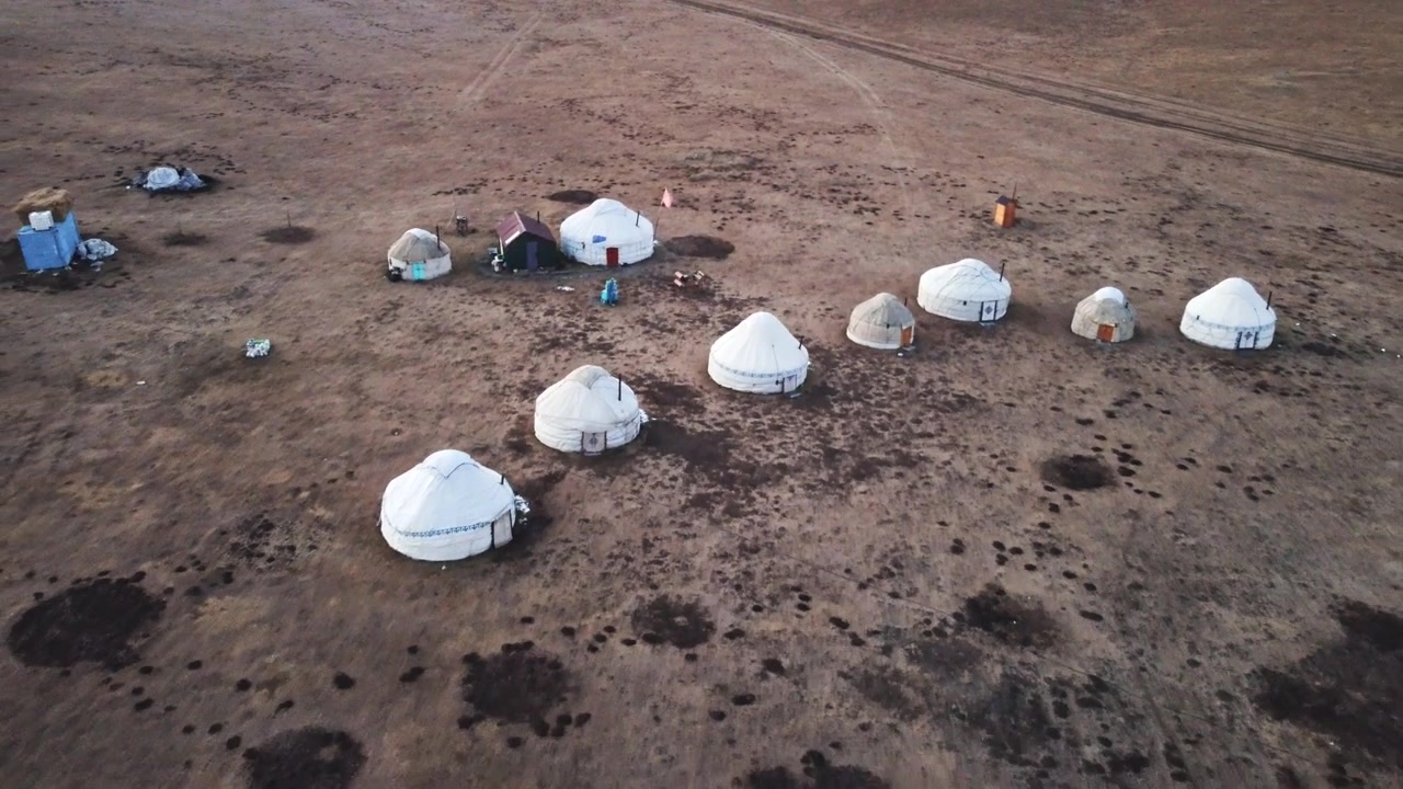 Aerial view of traditional white nomadic yurts on a vast green meadow near Song Köl lake, Kyrgyzstan. Authentic central asian nomadic culture and high altitude steppe landscape