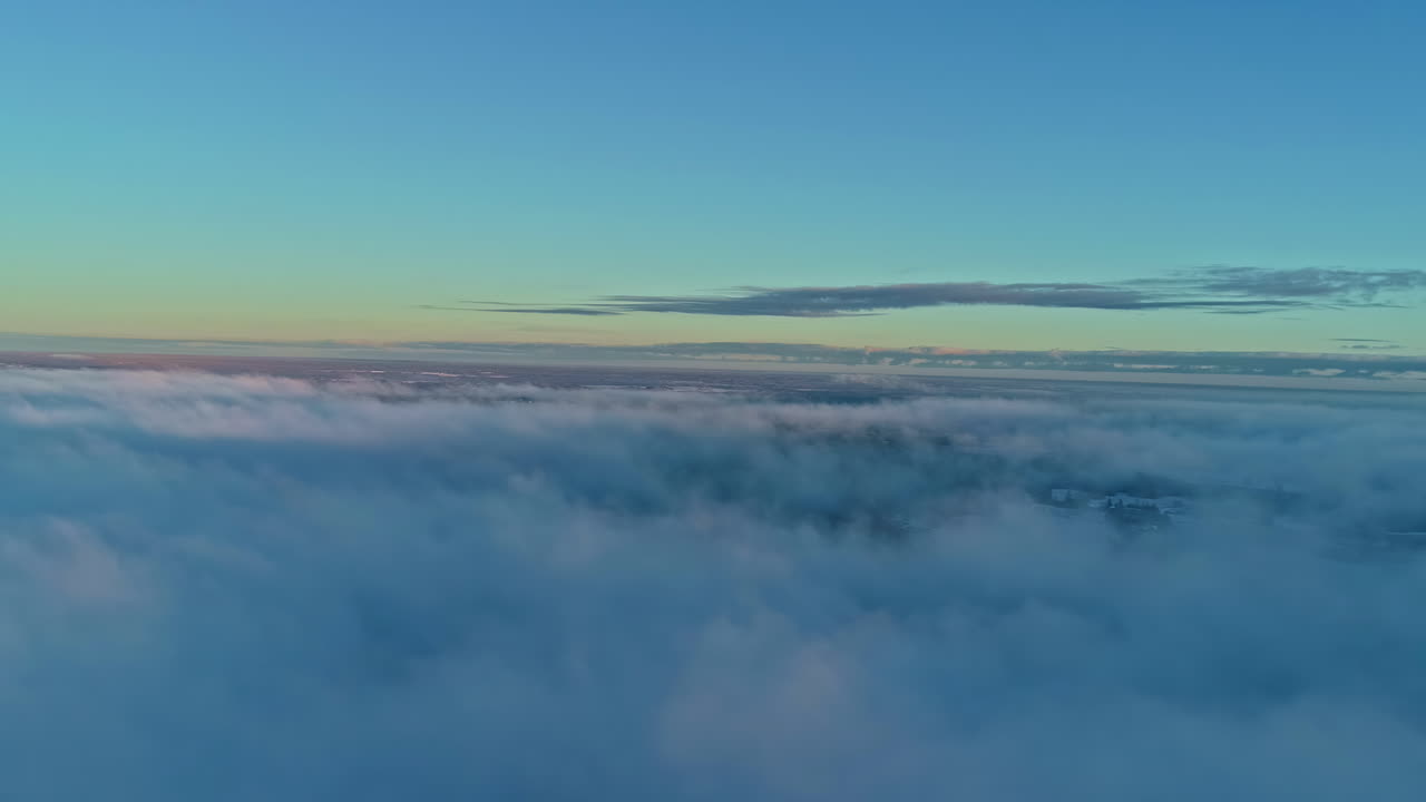 Inversion of fog or low-lying clouds cover the village landscape at dawn - aerial flyover above the clouds and misty fog