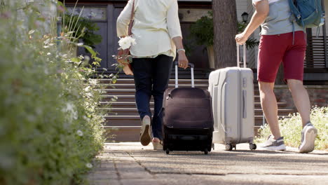 diverse senior couple walking with luggage to a house in sunny outdoors