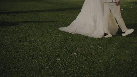 bride and groom walking on the grass at night, with the bride's gown trailing behind