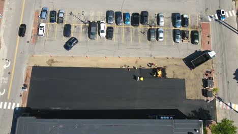 Time-lapse-drone-footage-of-a-work-crew-applying-asphalt-to-a-parking-lot,-looking-down-from-above