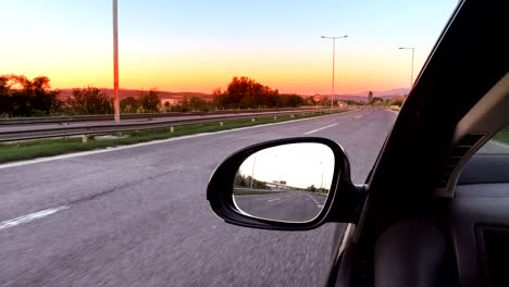 drive pov with view of car mirror on empty highway road towaard sunset, sunrise vibrant sky, cinematic look