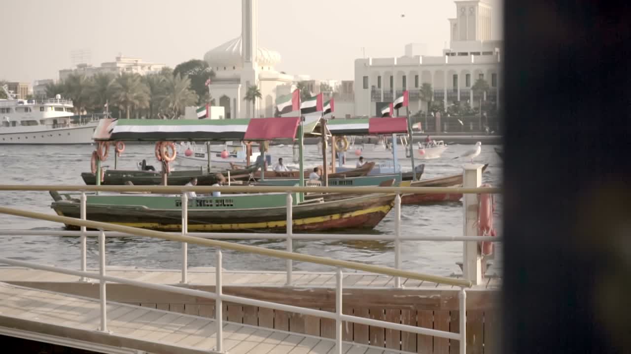 botes de madera con bandera emiratí al ralentí en el arroyo dubai mientras otros botes pasan en el fondo